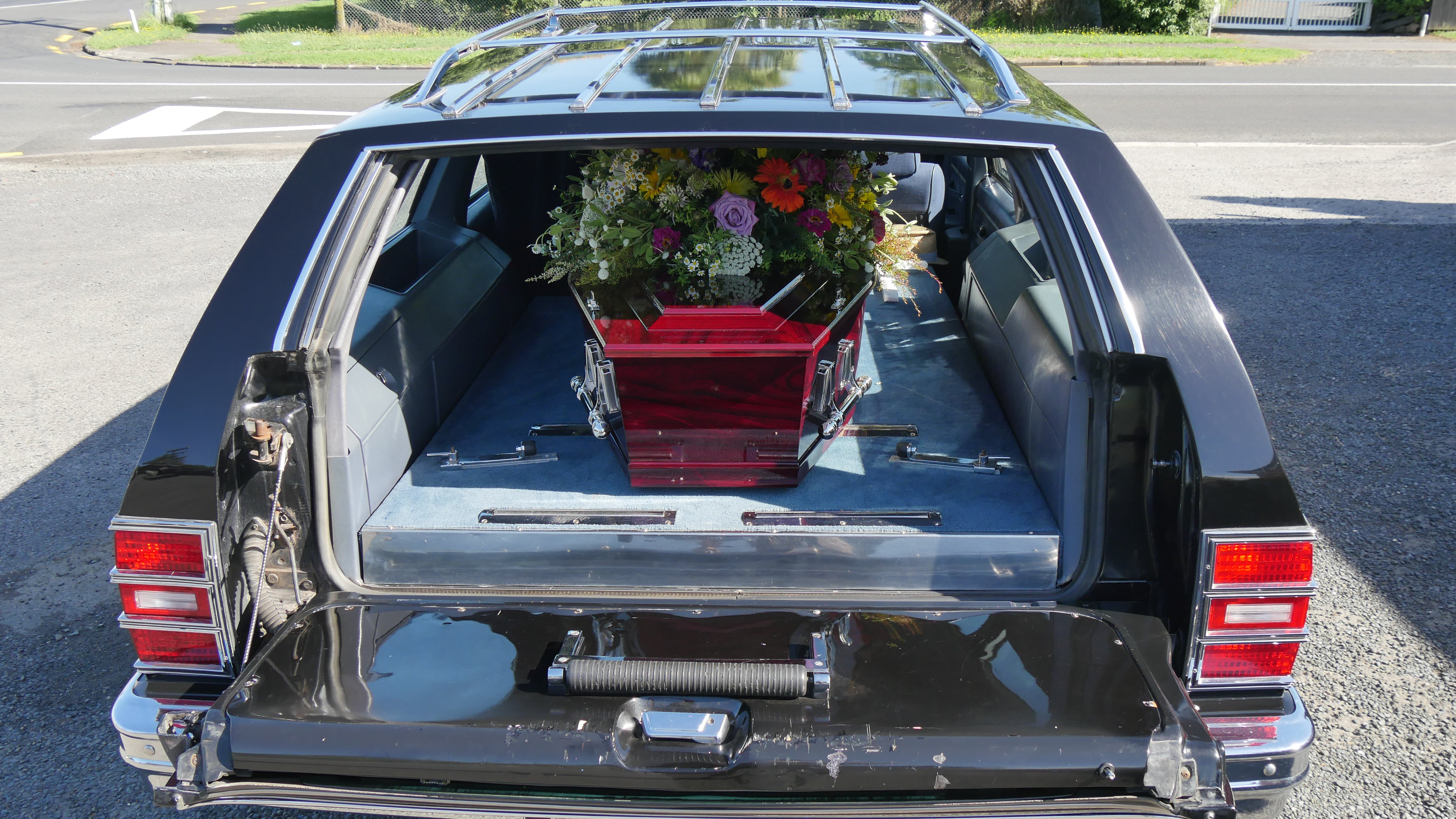 Funeral hearse with colorful flowers above casket.
