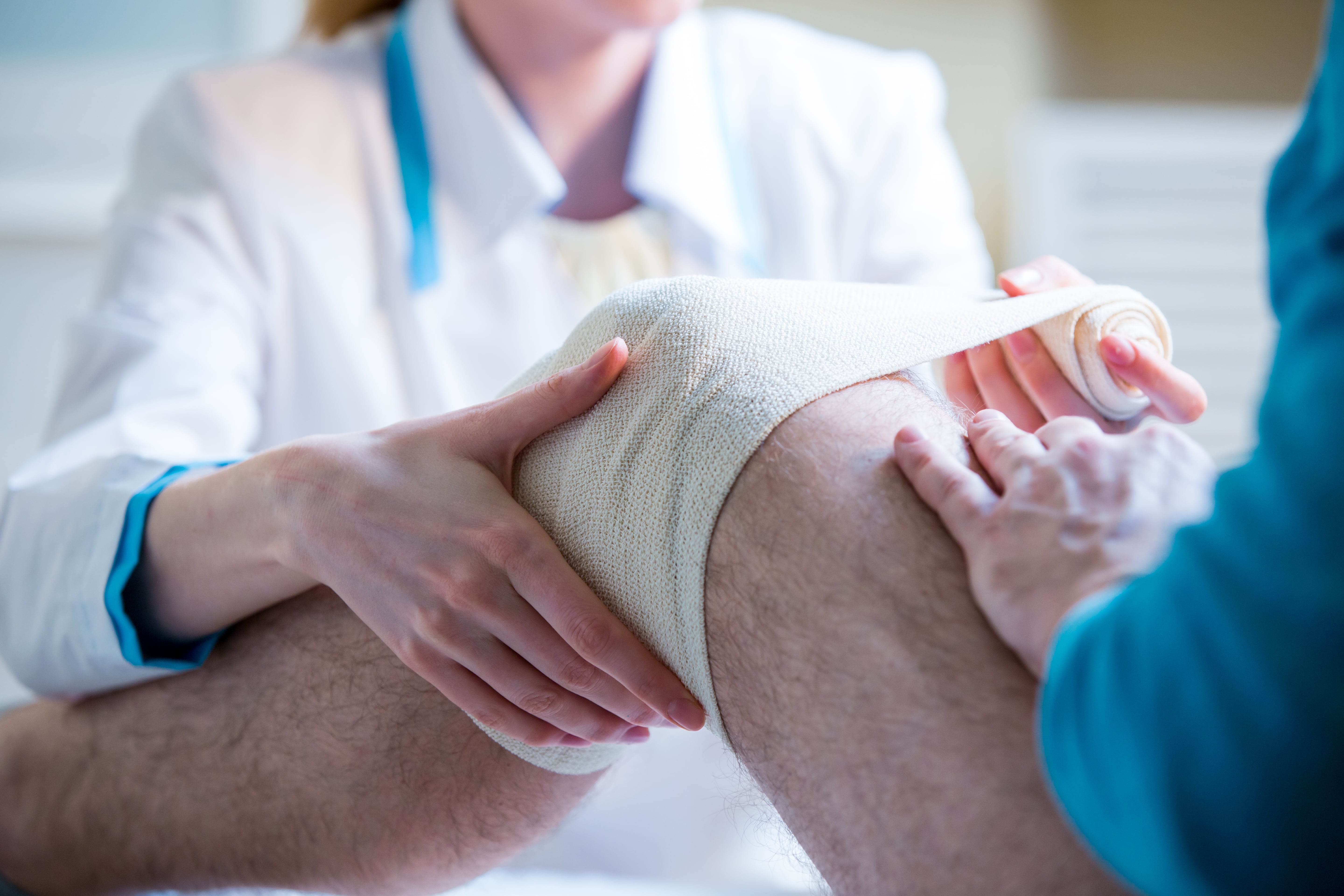 Doctor putting bandage on the patient's knee injury.